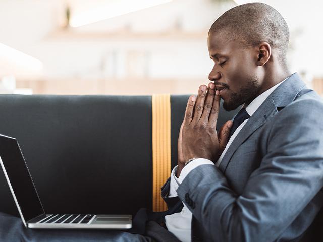 businessman saying a prayer with his laptop open and on his lap