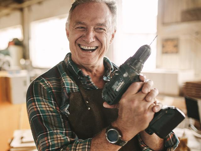 senior man smiling with power drill in his hand