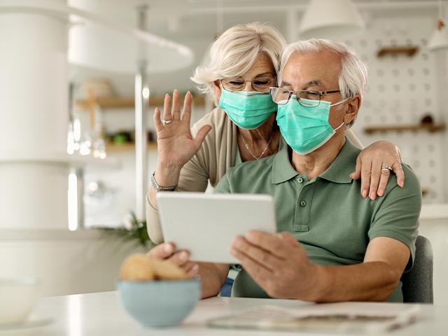 senior couple wearing facemasks and video chatting on tablet