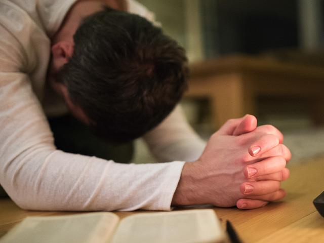 man kneeling and praying beside a Bible