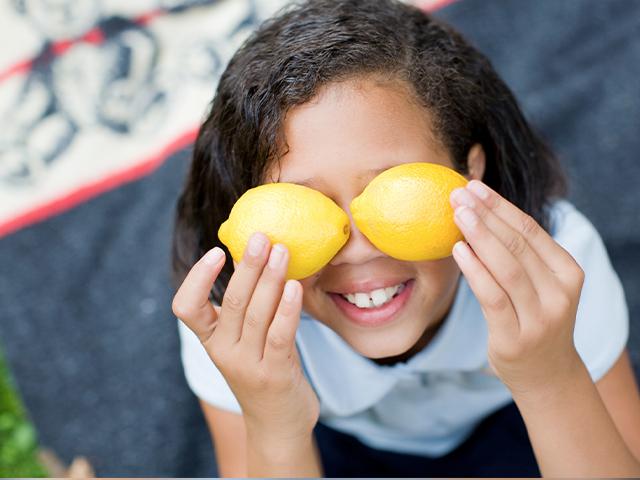 girl smiling and covering her eyes with bright yellow lemons