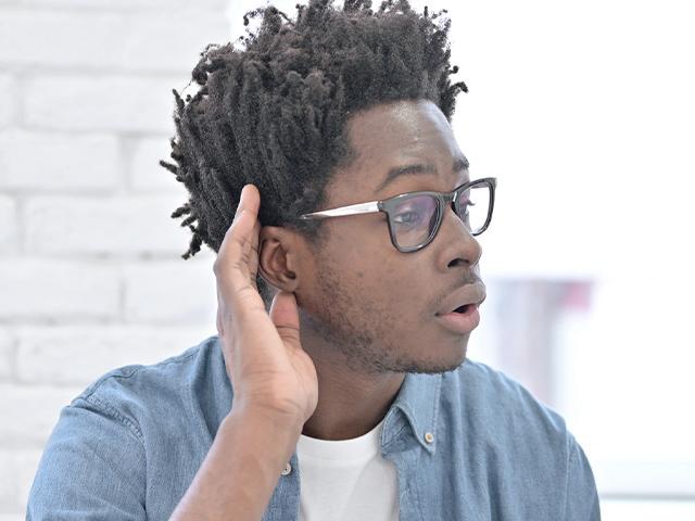 man with his hand cupped up to his ear to listen