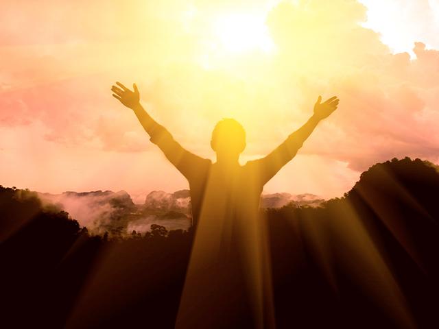 man thanks God with raised arms toward the light shining through the clouds