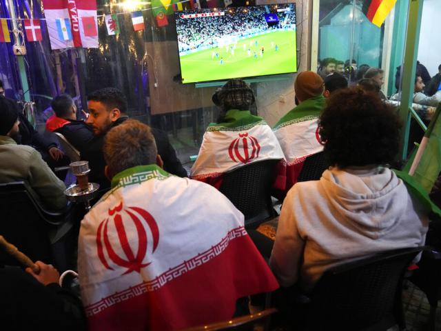 Lebanese soccer fans of Iran&#039;s team cover their backs with Iranian flags, as they sit at a coffee shop smoking water pipes and watch the World Cup in Beirut. (AP Photo/Hussein Malla)