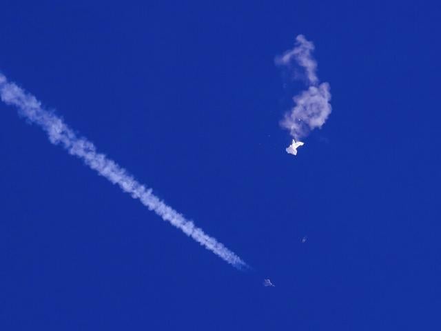 In this photo provided by Chad Fish, the remnants of a large balloon drift above the Atlantic Ocean, just off the coast of South Carolina, with a fighter jet and its contrail seen below it, Saturday, Feb. 4, 2023. (Chad Fish via AP)