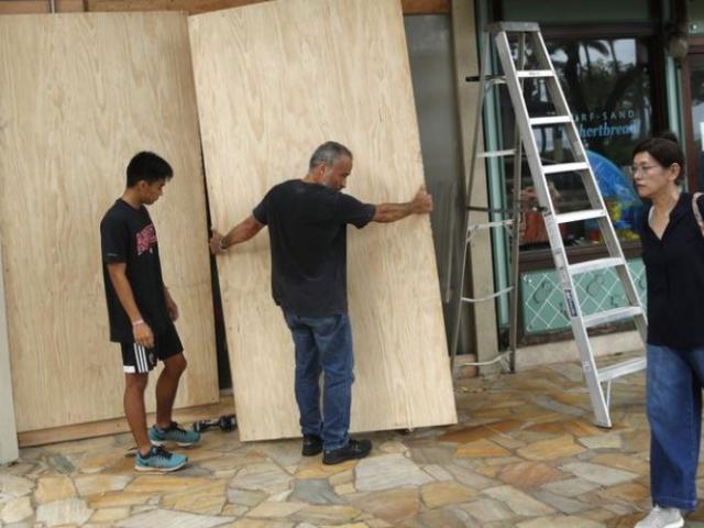 James Fujita, left, and Reid Fujita take down plywood boards that were to protect their store from Tropical Storm Lane along Waikiki Beach, Saturday. 