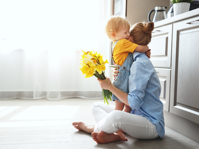 toddler boy gives mom flowers and a big hug