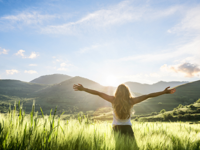 Woman facing the mountains and sunshine with arms wide open