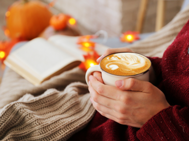 hands holding a cup of hot coffee in an autumn setting