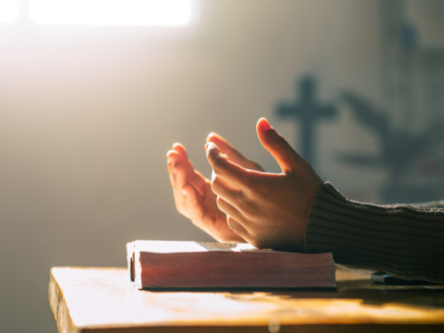 open hand prayer on a desk with a cross shadow on the wall