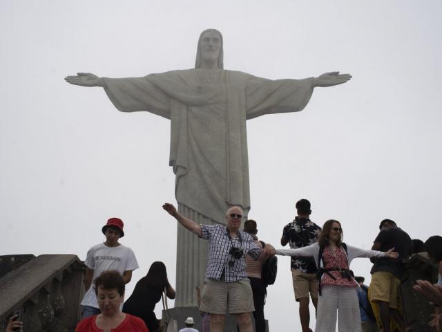 Tourists pose for photos in front of the Christ the Redeemer statue during a foggy day in Rio de Janeiro, Brazil (AP Photo/Silvia Izquierdo)