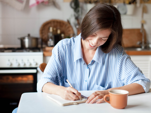 woman smiling and journaling with a coffee cup in front of her