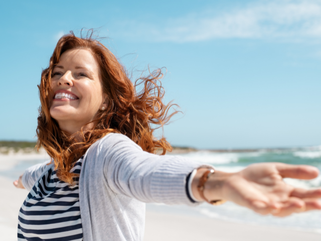 woman wearing a sweater and looking joyful on the beach 