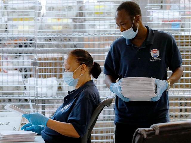 Workers wear personal protective equipment as they check ballots beside security cages at a Board of Elections facility, Wednesday, July 22, 2020, in New York. (AP Photo/John Minchillo)