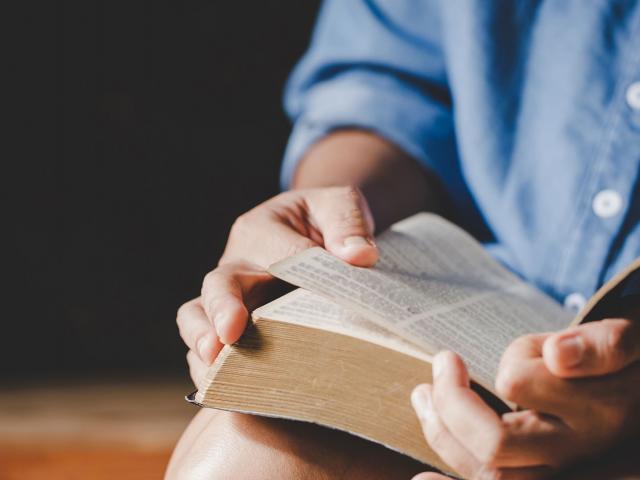 man sitting on a wooden bench reading a Bible