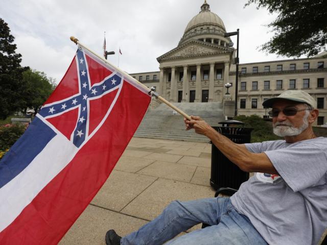 Larry Eubanks waves the current Mississippi state flag as he sits before the front of the Capitol on June 27, 2020, in Jackson, Miss. (AP Photo/Rogelio V. Solis)