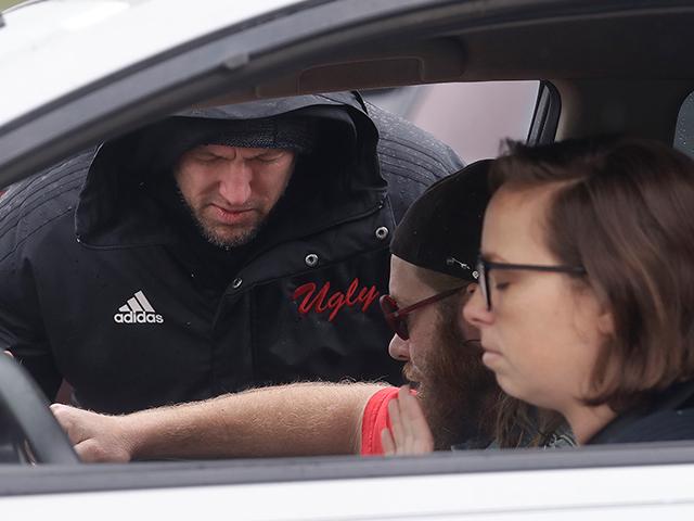 Executive pastor Jason Bishop, rear, closes his eyes while delivering drive up prayer service to Samantha Ferro, right, and Bobby Hallman in their car outside of The Bay Church in Concord, Calif., Sunday, March 15, 2020. (AP Photo/Jeff Chiu)