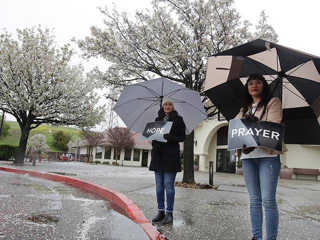 Martha Valdivia, left, and Maria Munoz wait for cars to offer drive up prayer service outside of The Bay Church in Concord, Calif., Sunday, March 15, 2020. (AP Photo/Jeff Chiu)