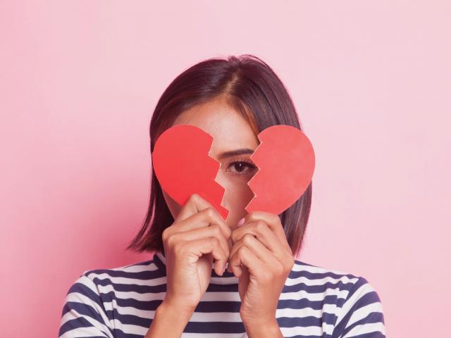 Woman in striped shirt against pink wall holding broken paper heart