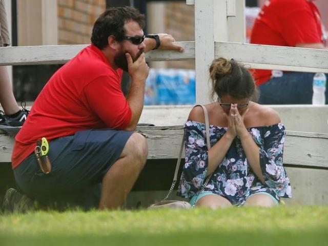 A woman prays in the grass outside the Alamo Gym where parents wait to reunite with their kids following a shooting at Santa Fe High School Friday, May 18, 2018, in Santa Fe, Texas.