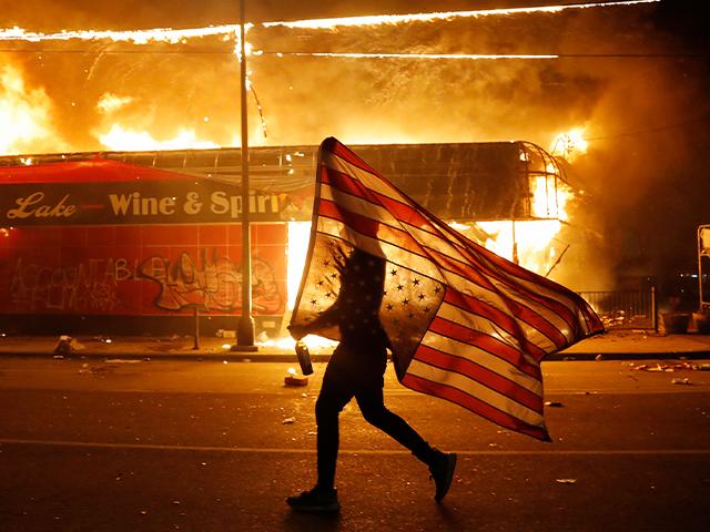 A protester carries a U.S. flag upside down next to a burning building May 28, 2020, in Minneapolis in protests over the death of George Floyd, a black man who died in police custody. (AP Photo/Julio Cortez)