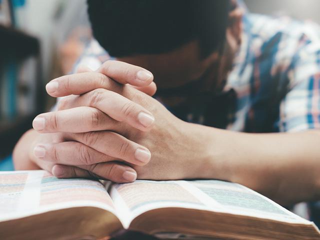 man praying with hands overtop an open Bible