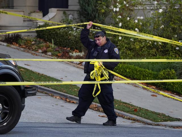 A police officer rolls out more yellow tape on the closed street below the home of House Speaker Nancy Pelosi and her husband Paul Pelosi in San Francisco, Oct. 28, 2022. (AP Photo/Eric Risberg)