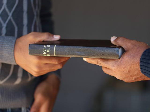 older man handing younger man a Bible