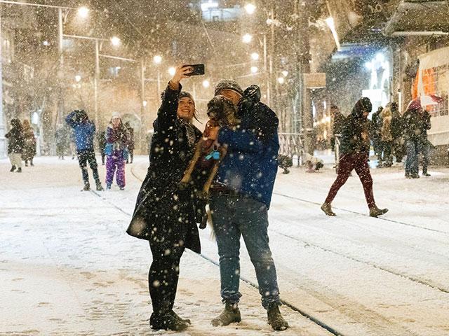 A couple takes a selfie with their dog as snow falls near the Machane Yehuda market in central Jerusalem, Wednesday, Jan. 26, 2022. Photo Credit: AP Photo/Maya Alleruzzo