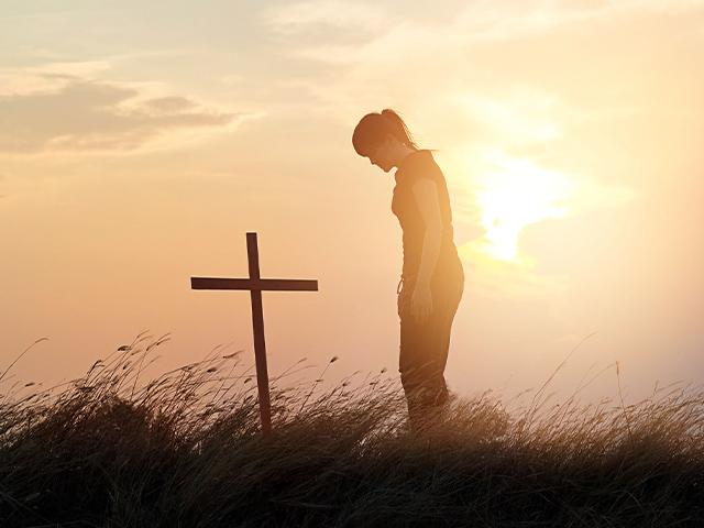 woman showing respect for the cross on a hill at sunset