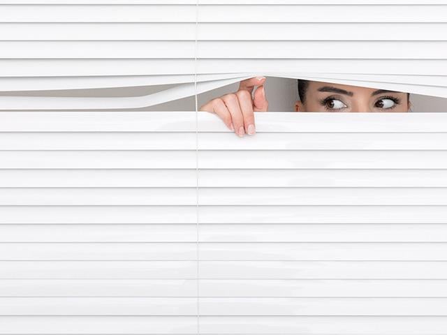woman peeking out from her window blinds