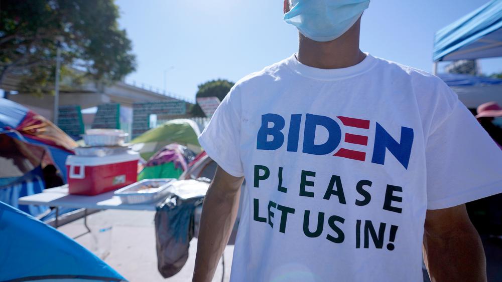A Honduran man seeking asylum in the U.S. wears a shirt that reads, &quot;Biden please let us in,&quot; as he stands near an entrance to the border crossing, March 1, 2021, in Tijuana, Mexico. (AP Photo/Gregory Bull)