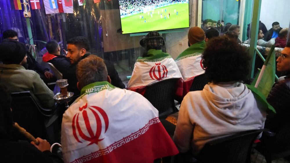 Lebanese soccer fans of Iran&#039;s team cover their backs with Iranian flags, as they sit at a coffee shop smoking water pipes and watch the World Cup in Beirut. (AP Photo/Hussein Malla)