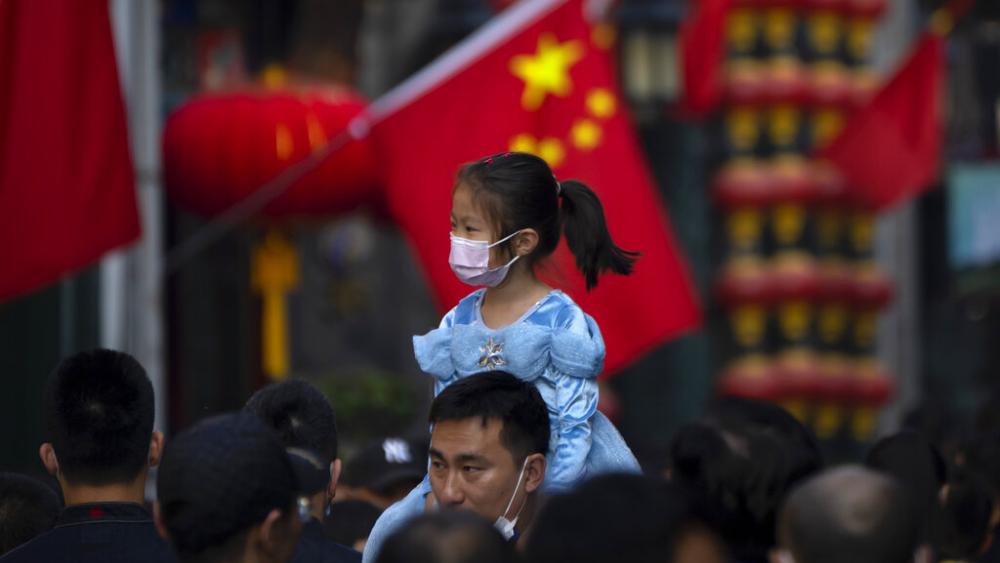 A girl wearing a face mask rides on a man&#039;s shoulders as they walk along a tourist shopping street in Beijing on Oct. 7, 2022. China has announced its first overall population decline in recent years. (AP Photo/Mark Schiefelbein, File)