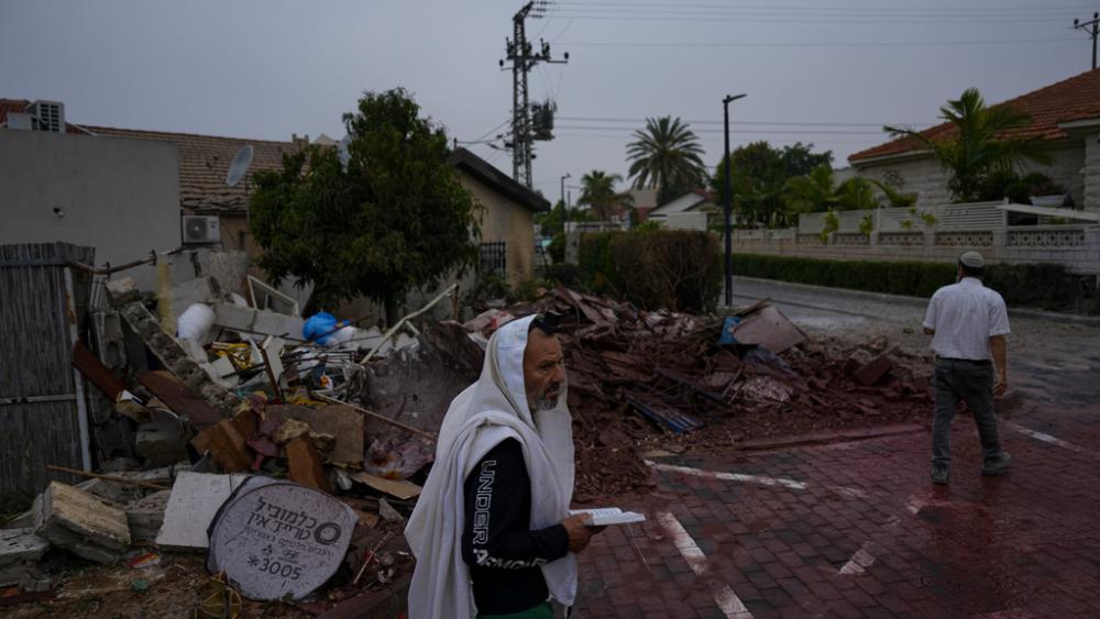 A man covered in a prayer shawl holds a holy book as he stands by a structure destroyed by a rocket fired Wednesday from the Gaza Strip by Palestinian militants, in Ashkelon, Israel, Thursday, May 11, 2023. (AP Photo/Ariel Schalit)
