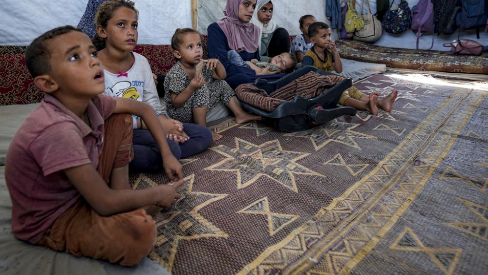 Displaced infant Abdel-Rahman Abu El-Jedian, 11-month-old, who suffers from polio, is carried by his mother, center, at a makeshift tent camp in Deir al-Balah, central Gaza Strip, Tuesday, Aug. 27, 2024. (AP Photo/Abdel Kareem Hana)