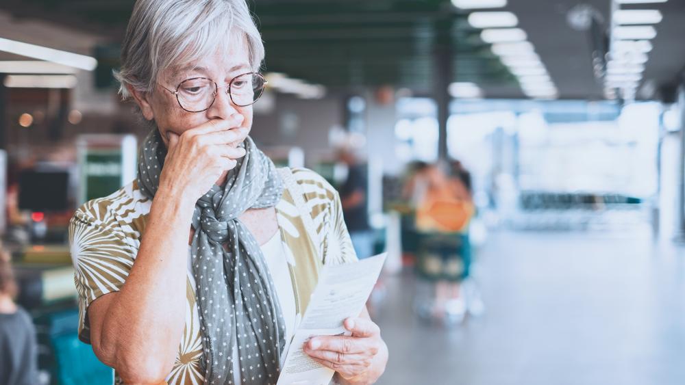 Senior woman in the supermarket checks her grocery receipt looking worried about rising costs (Adobe stock)