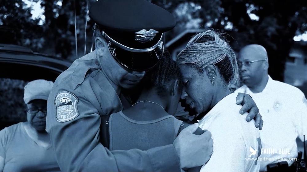 A police officer prays with grieving citizens.