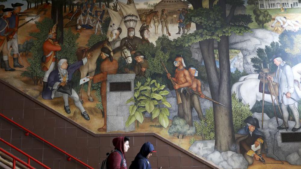In this photo taken April 3, 2019, a pair of students walk past a historic mural that includes slaves and a dead Native American at George Washington High School in San Francisco. (Yalonda M. James/San Francisco Chronicle via AP) 