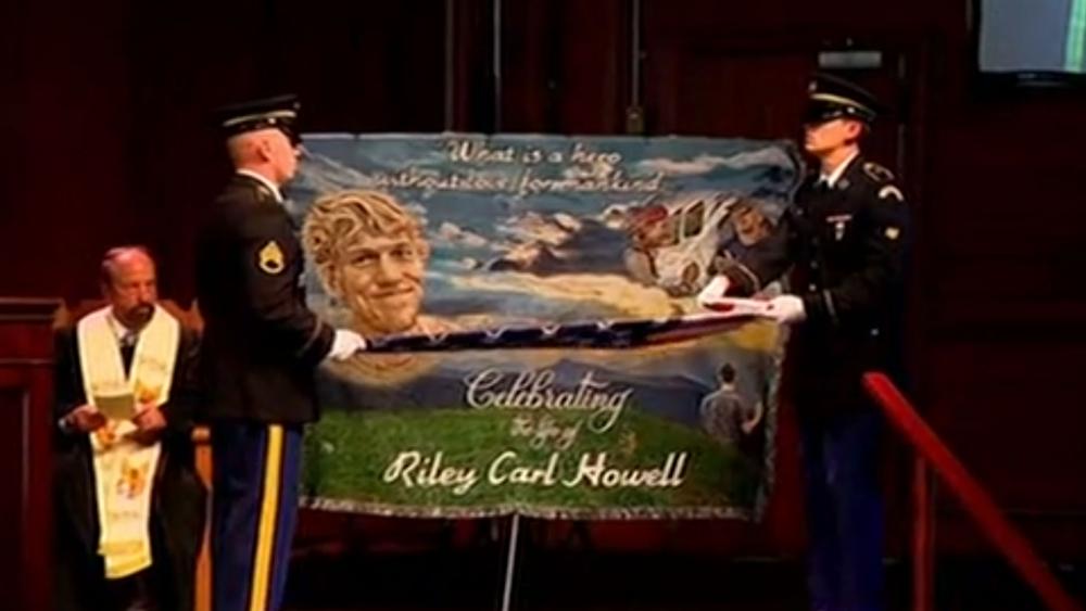 A military honor guard folds the American flag in front of an image of Riley Howell at his funeral Sunday. (Screenshot credit: APTN) 