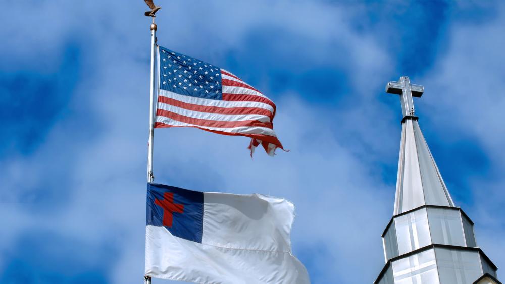 An American flag and Christian flag fly near a church steeple with a cross (Adobe Stock image)