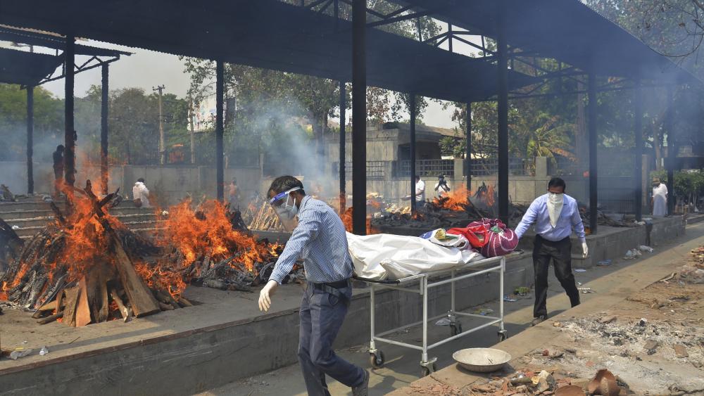 In this May 1, 2021, file photo, relatives carry the body of a person who died of COVID-19 as multiple pyres of other COVID-19 victims burn at a crematorium in New Delhi, India. (AP Photo/Amit Sharma, File)