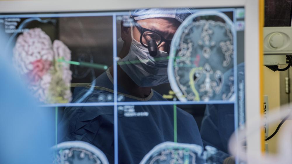 In this 2017 photo provided by the University of California, San Francisco, neurosurgeon Dr. Edward Chang is reflected in a computer monitor displaying brain scans as he performs surgery at UCSF. (Barbara Ries/UCSF via AP)