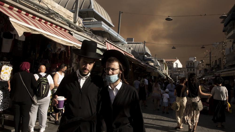 Ultra-Orthodox Jews stroll through the Machane Yehuda market under a sky darkened by nearby wildfires, in Jerusalem, Sunday, Aug. 15, 2021.(AP Photo/Maya Alleruzzo)