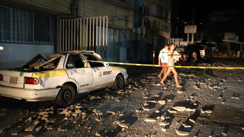 A couple walks past a taxi cab that was damaged by falling debris after a strong earthquake in Acapulco, Mexico, Tuesday, Sept. 7, 2021. (AP Photo)
