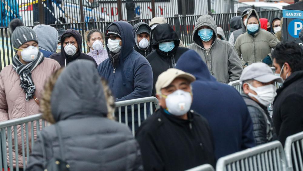 Patients wear personal protective equipment while maintaining social distancing as they wait in line for a COVID-19 test at Elmhurst Hospital Center, March 25, 2020, in New York (AP Photo/John Minchillo)