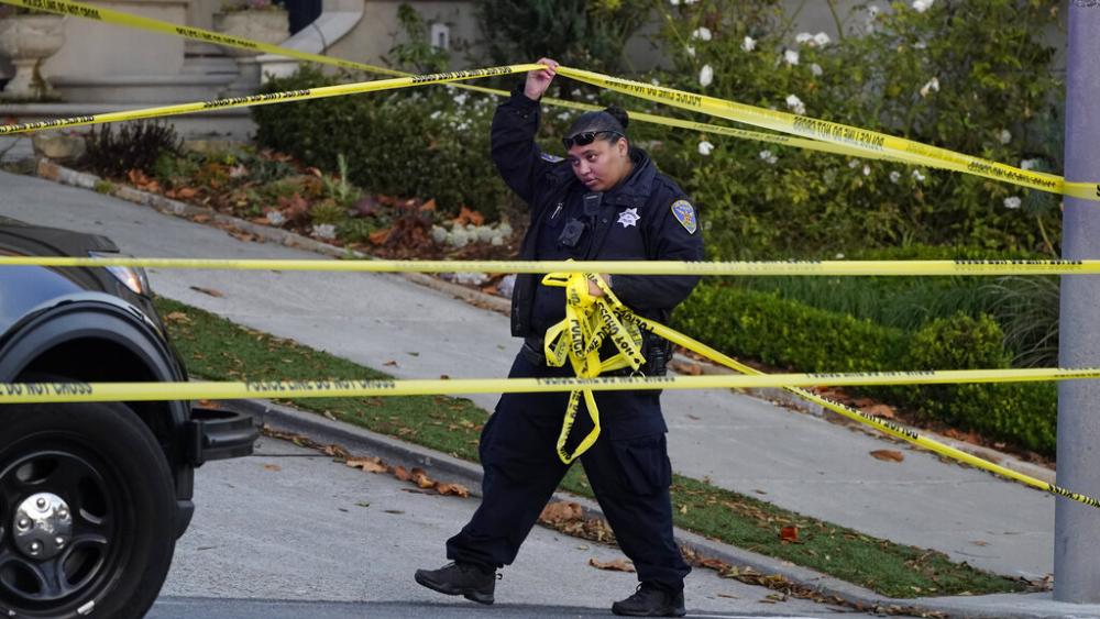 A police officer rolls out more yellow tape on the closed street below the home of House Speaker Nancy Pelosi and her husband Paul Pelosi in San Francisco, Oct. 28, 2022. (AP Photo/Eric Risberg)