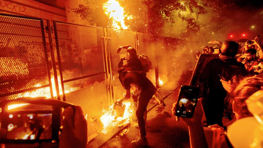 Protesters throw flaming debris over a fence at the Mark O. Hatfield US Courthouse in Portland, Ore. (AP Photo/Noah Berger)