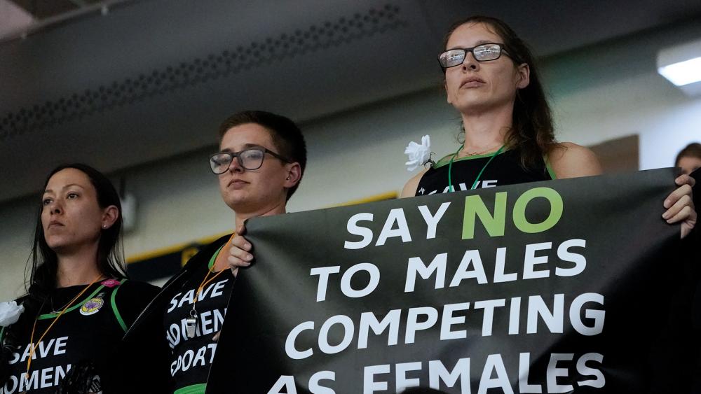 Protesters stand as Pennsylvania transgender athlete Lia Thomas competes in the women&#039;s 200 freestyle final at the NCAA swimming and diving championships, March 18, 2022 (AP Photo/John Bazemore)